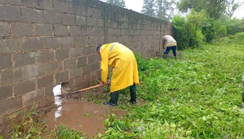 Un operario con impermeable amarillo y pala destapa un orificio en la base de un paredón de bloques junto a un bañado.