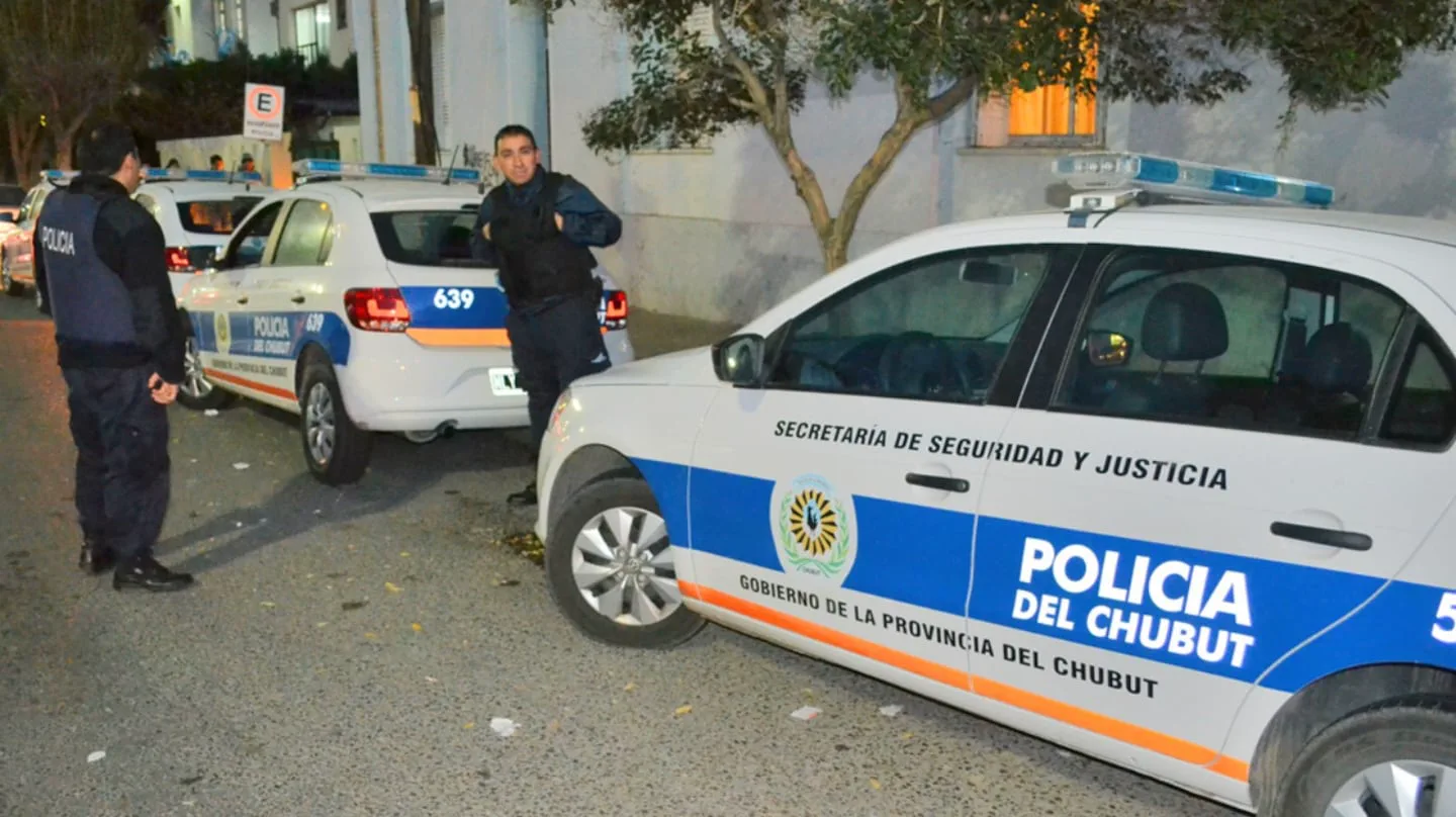 Efectivos policiales junto a patrulleros de la Policía del Chubut estacionados en la calle por la noche.