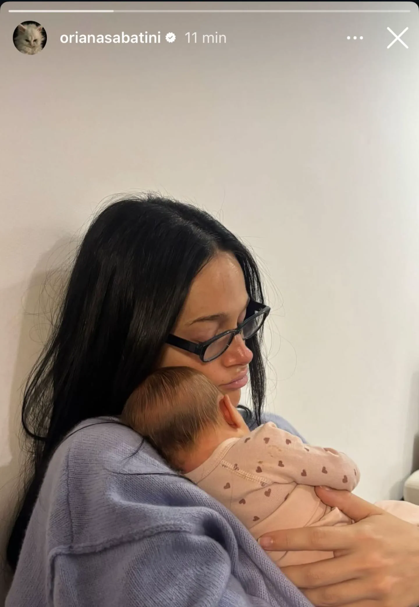Oriana Sabatini sosteniendo a un bebé en brazos contra una pared clara.