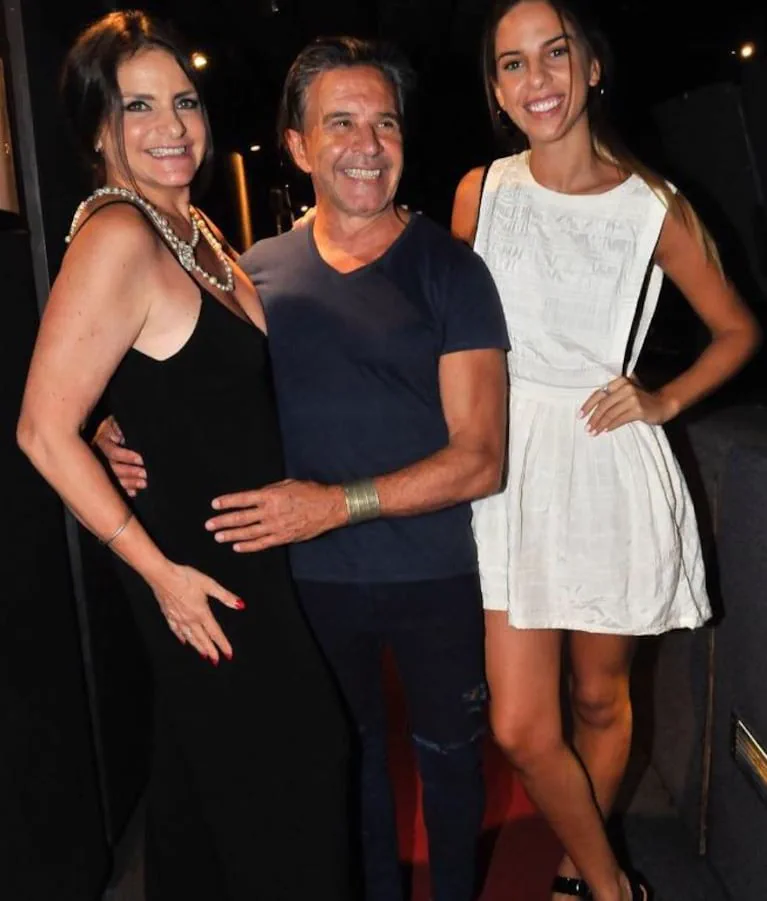 Un hombre y dos mujeres posan sonrientes y abrazados vestidos de fiesta.
