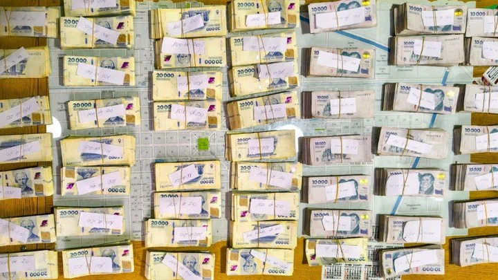 Fajos de billetes argentinos acomodados sobre una mesa con papeles blancos encima.