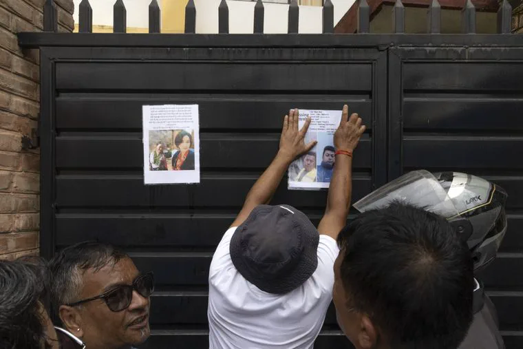 Una persona pega carteles de personas desaparecidas sobre un porton negro frente a otros dos hombres.