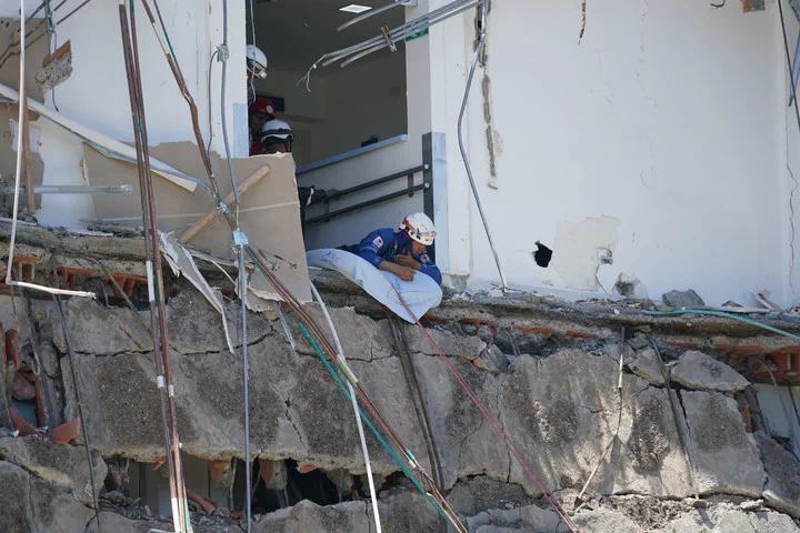 Rescatistas con casco sobre los restos colapsados y agrietados de un edificio danado.