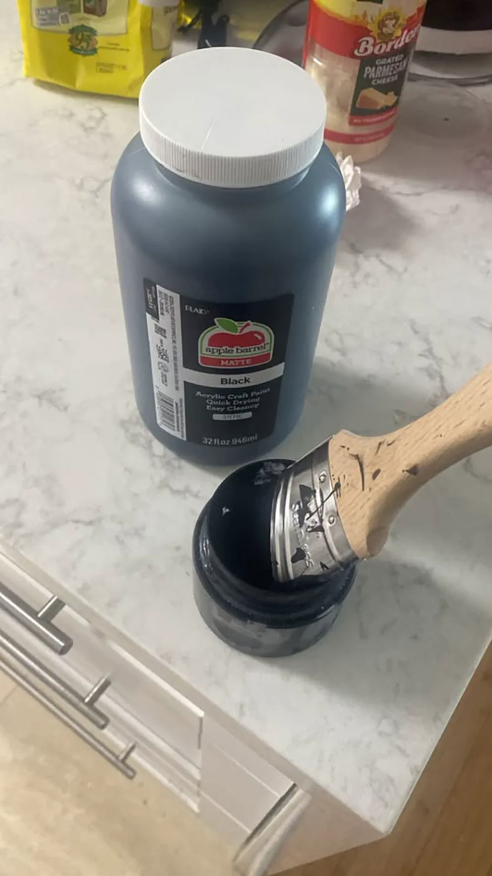 Pincel metido en un pote con pintura negra junto a un frasco grande sobre una mesada de cocina.