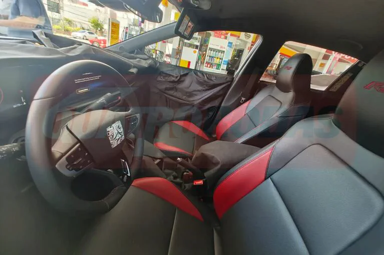 El habitáculo de un auto muestra el volante, el torpedo parcialmente tapado y butacas tapizadas en negro y rojo.