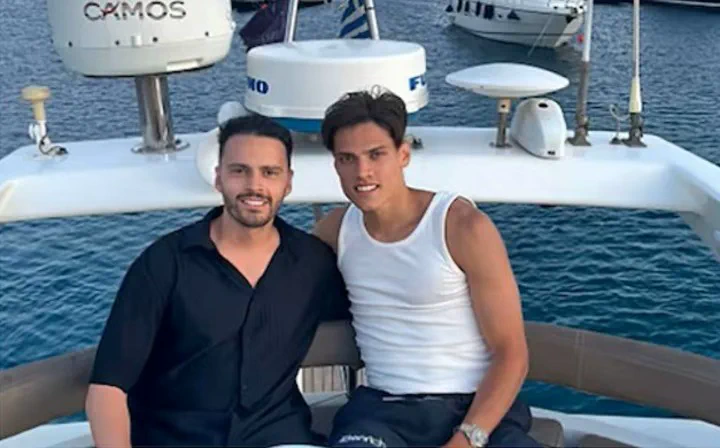 Dos hombres sentados a bordo de una embarcacion sonrien mirando a la camara con el mar de fondo.