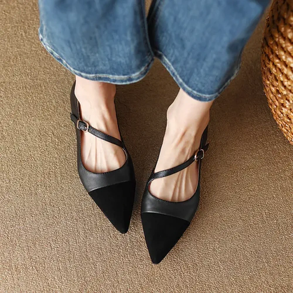 Pies de una persona que viste jeans y calza zapatos negros en punta con correa cruzada y hebilla.