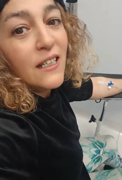 Una mujer sentada en una sala médica con una vía intravenosa colocada en el brazo.