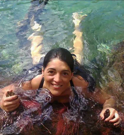 Una mujer sumergida en el agua sonríe mientras se sostiene de las rocas.