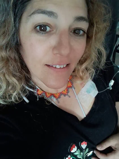 Una mujer sonríe a la cámara llevando puesto un collar colorido y una sonda sujeta al pecho.