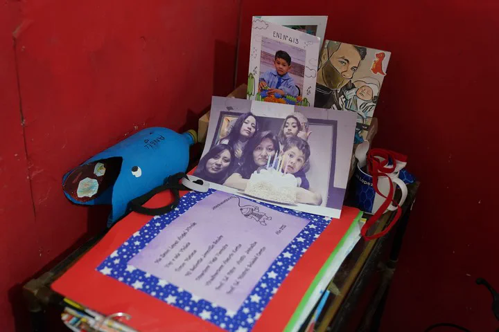 Un mueble con fotos de un nene y su familia, una botella de plástico decorada y una carpeta escolar.
