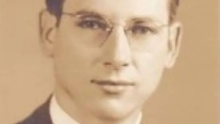 Retrato sepia en plano medio de un hombre joven con anteojos y saco.