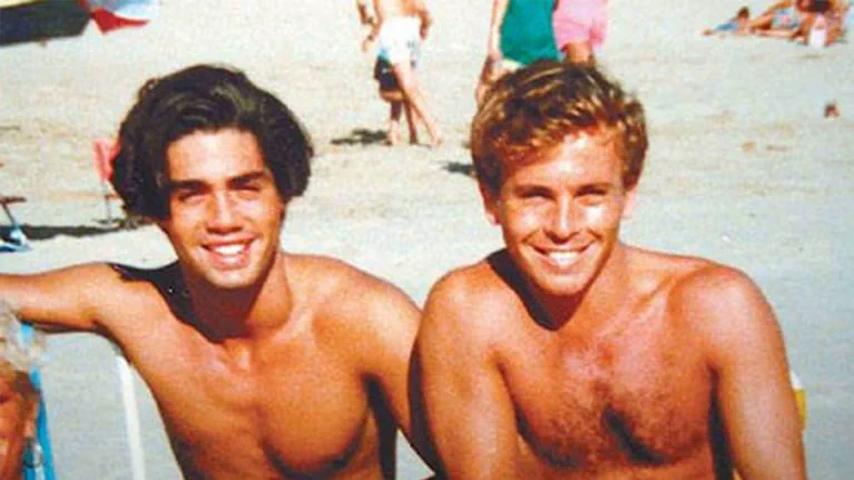 Ricardo Fort y Guido Suller jovenes y sonrientes sin remera en la playa.