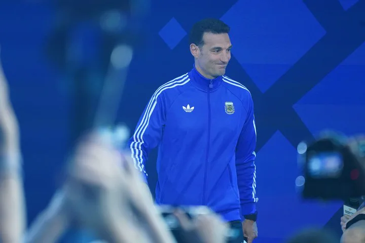 Lionel Scaloni sonríe con una campera azul de la selección argentina frente a varias cámaras.