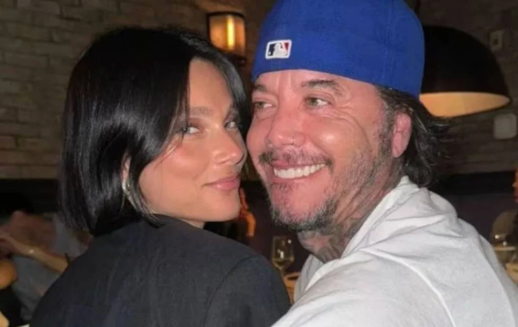 Sebastián Ortega con gorra azul y una mujer sonriendo juntos de perfil en un restaurante.