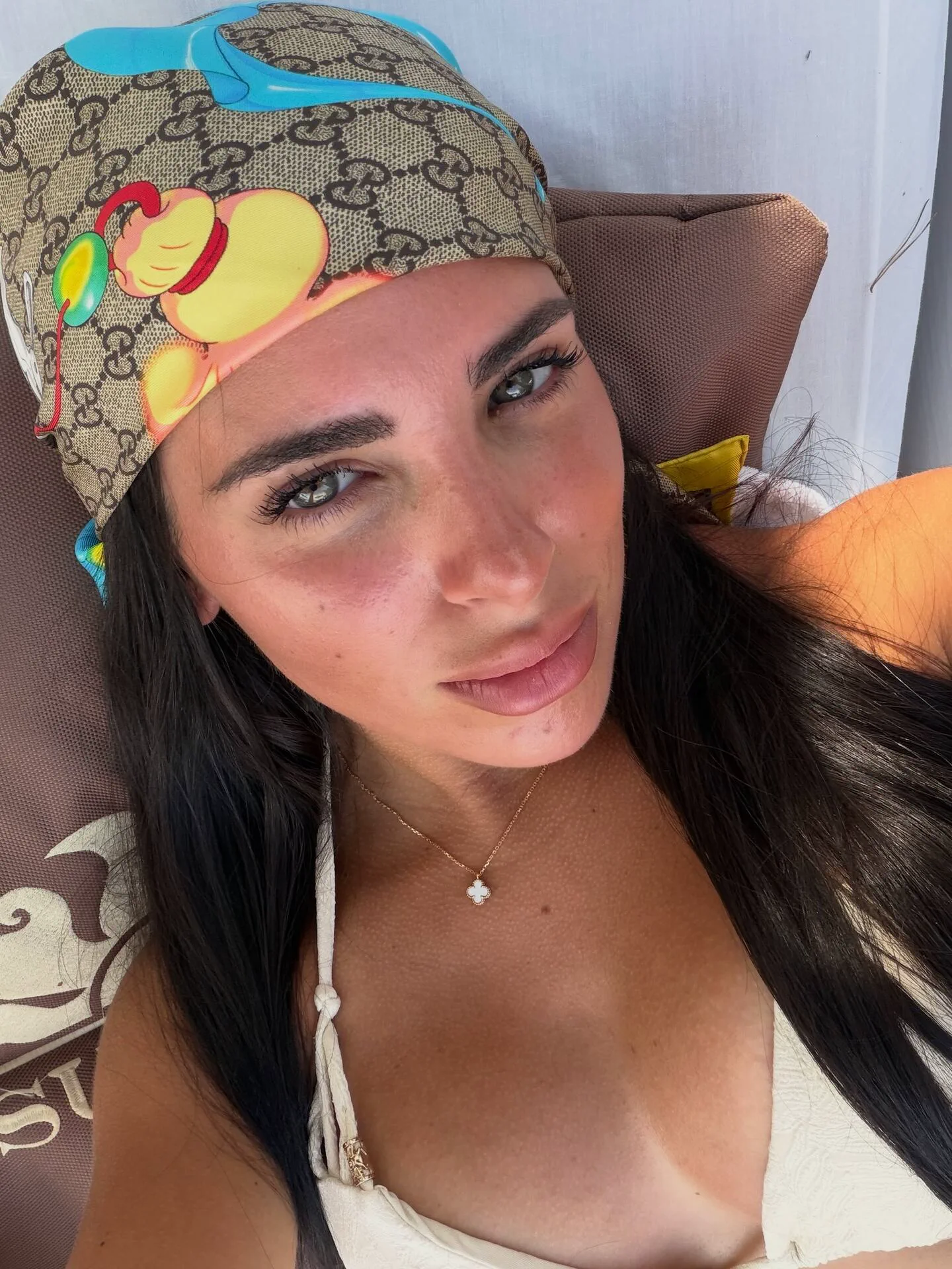 Una mujer recostada en una reposera se saca una selfie en primer plano con un pañuelo en la cabeza.