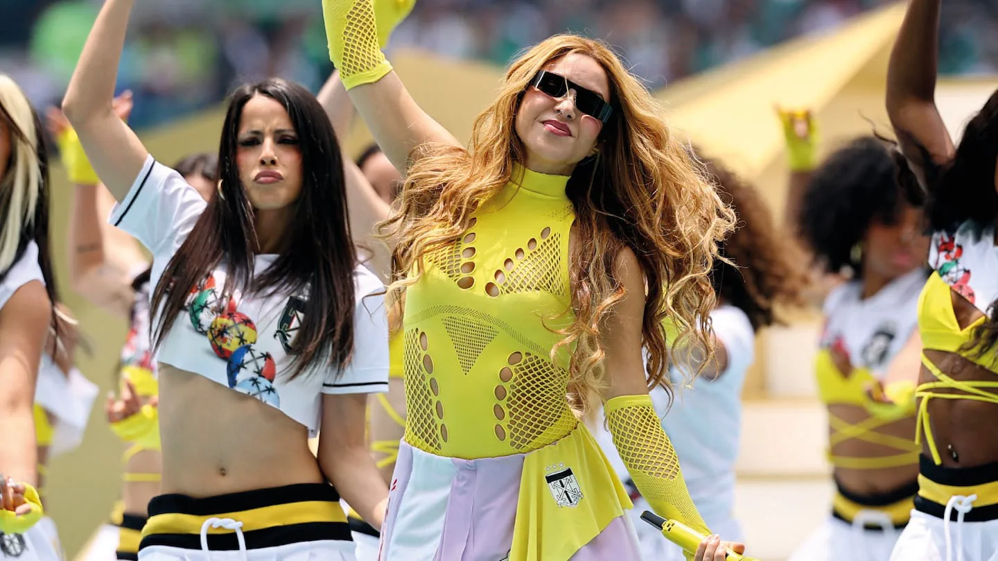 La cantante Shakira vestida de amarillo cantando junto a sus bailarinas en un show en vivo.