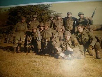 Un grupo de soldados uniformados posa en el pasto al aire libre junto a unos arboles.