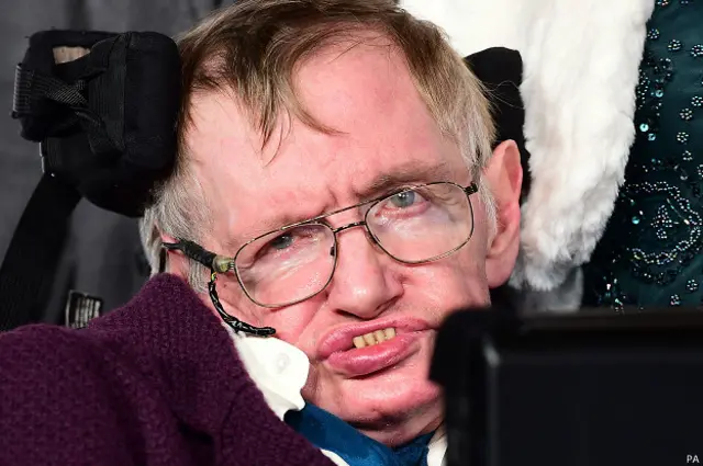 Stephen Hawking en su silla de ruedas con anteojos y saco bordo.