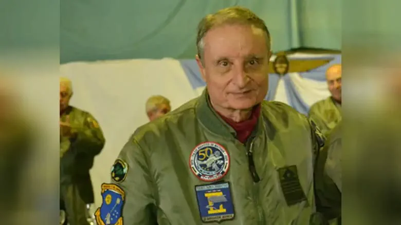 Un hombre sonríe vistiendo una campera militar verde con insignias de la Fuerza Aérea.