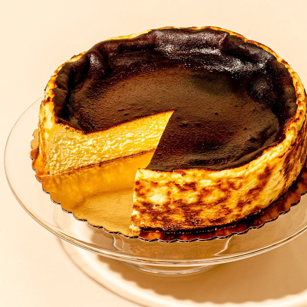 Una tarta de queso quemada vasca a la que le falta una porción está apoyada sobre una base de vidrio.