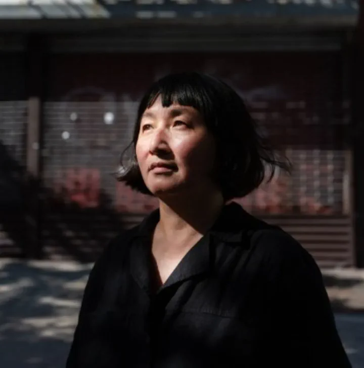 Retrato al aire libre de una mujer de cabello corto y oscuro vestida de negro bajo la luz del sol.