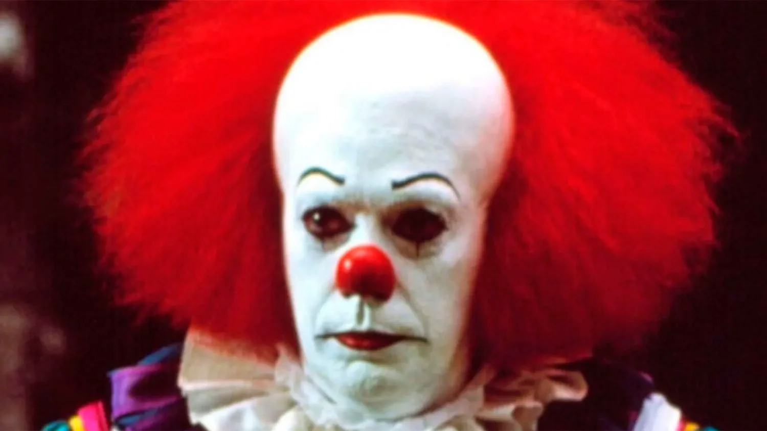 Un hombre caracterizado como payaso con pelo rojo, cara pintada de blanco y nariz roja.