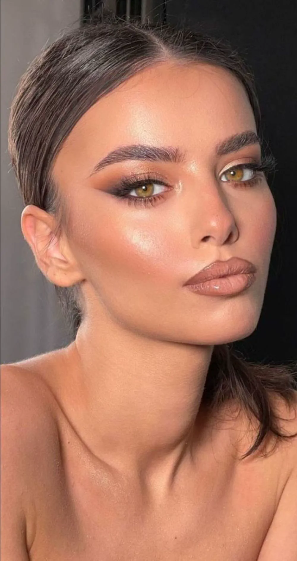 Una mujer joven posa en primer plano con maquillaje en tonos marrones y labios con brillo.