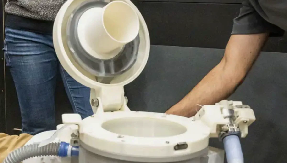 Un inodoro espacial blanco abierto manipulado por una persona.