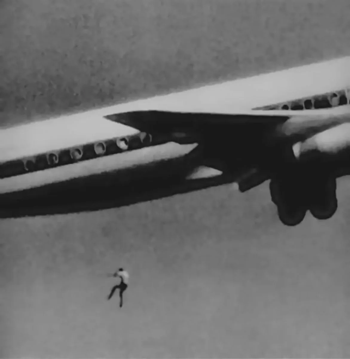 Un hombre cae al vacio debajo del fuselaje y el ala de un avion comercial en pleno vuelo.