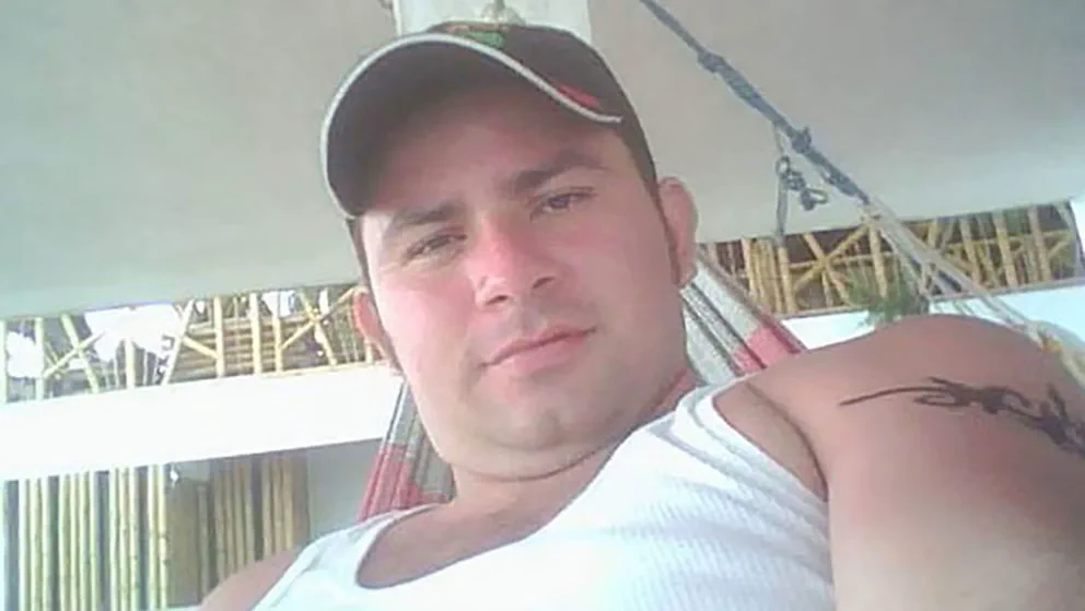 Un hombre con gorra y musculosa blanca descansa recostado en una hamaca paraguaya.