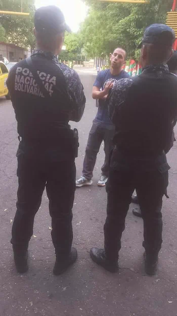 Un hombre conversa en la calle frente a dos efectivos de la Policia Nacional Bolivariana de espaldas.