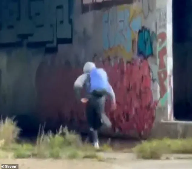 Una persona de espaldas con capucha y mochila azul corre frente a una pared con grafitis.