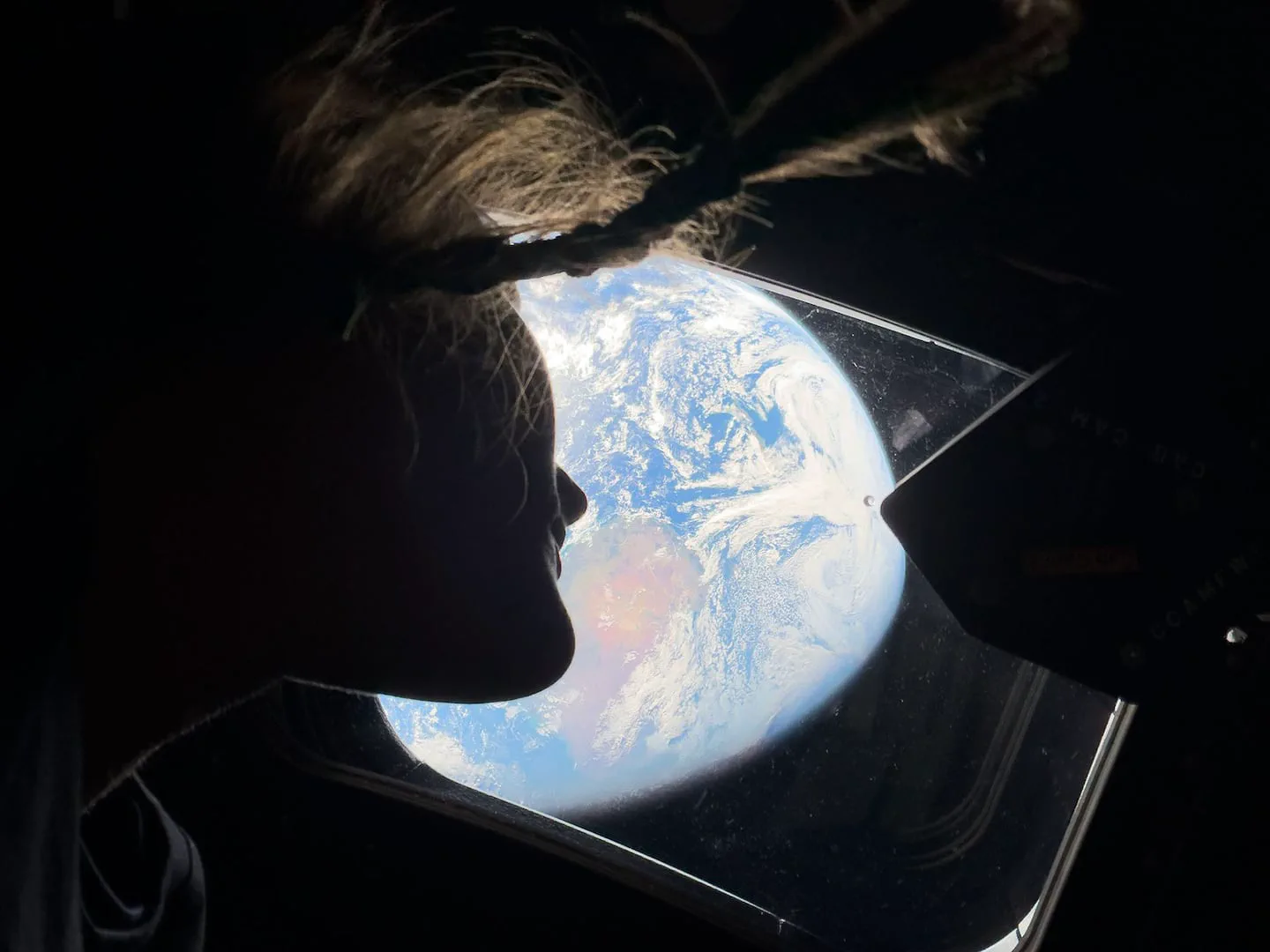 Silueta del perfil de una persona mirando el planeta Tierra iluminado a traves de la ventanilla de una nave espacial.