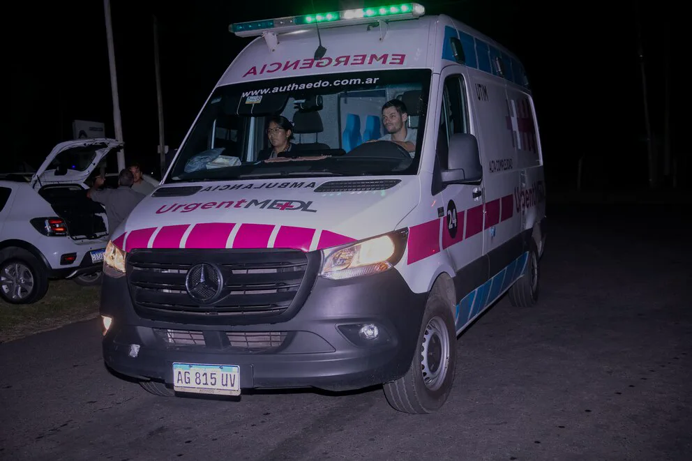 Una ambulancia de traslados medicos avanza de noche con dos personas en la cabina y las luces encendidas.