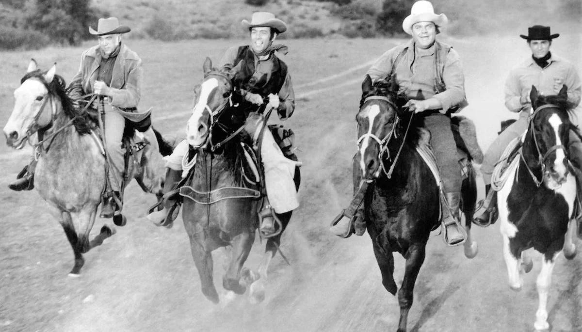 Los personajes de la serie Bonanza cabalgando a caballo al trote en una toma en blanco y negro.