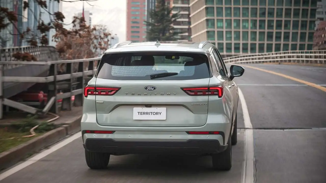 Camioneta Ford Territory color claro vista desde atrás circulando por un puente o autopista urbana.