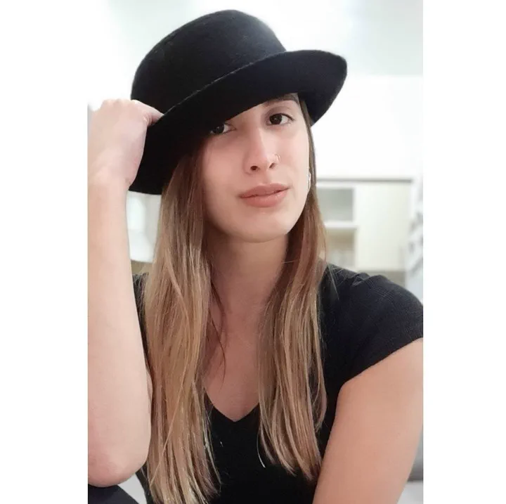 Una joven con remera negra posa sosteniendo un sombrero negro sobre su cabeza.