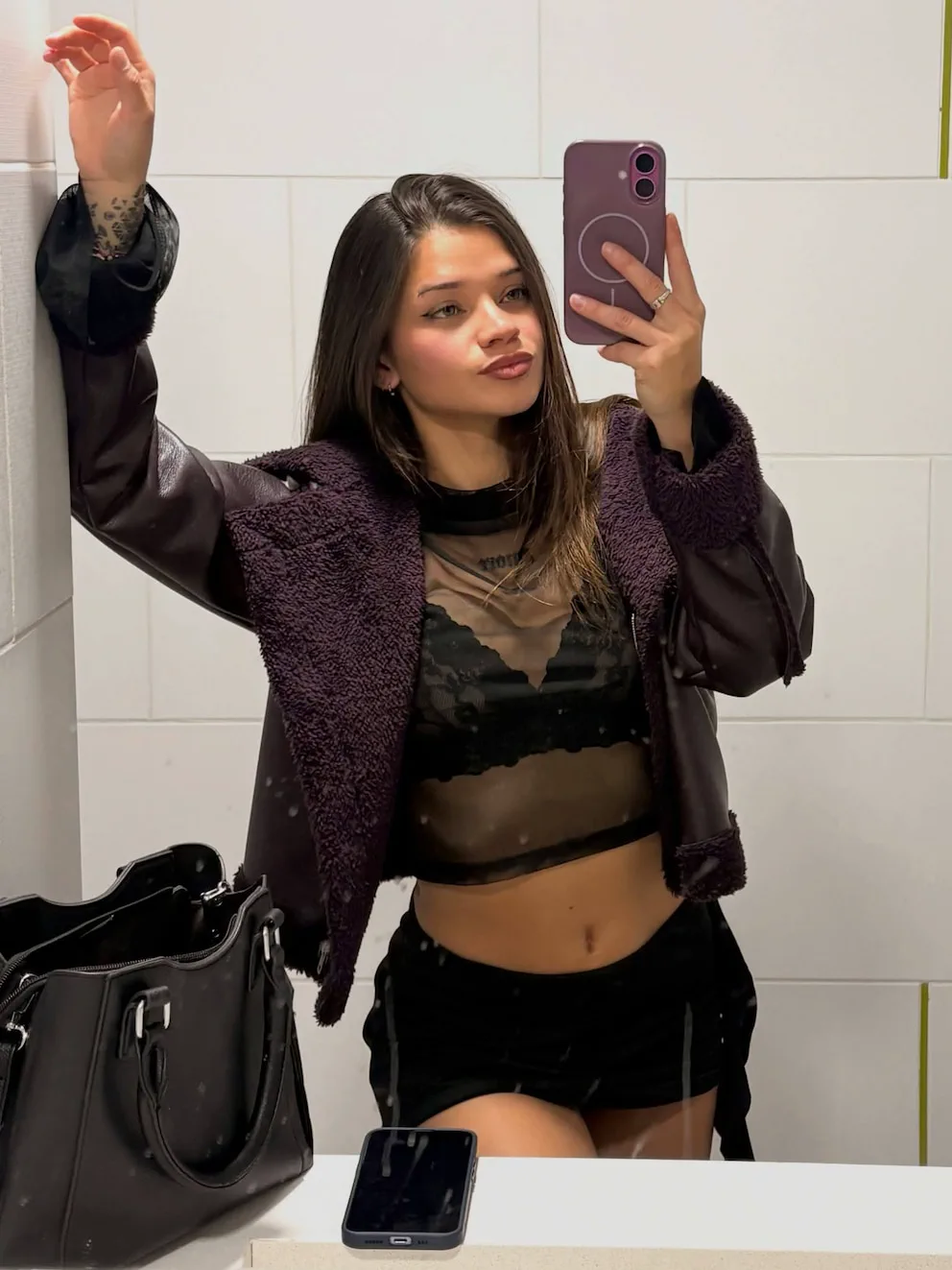 Una joven se saca una selfie en el espejo con campera de abrigo y top transparente.