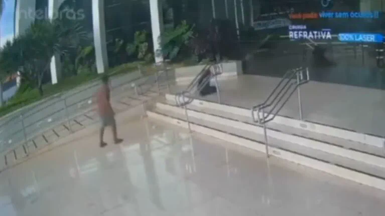Una persona camina frente a una escalinata con barandas metalicas en la entrada de un edificio vidriado.