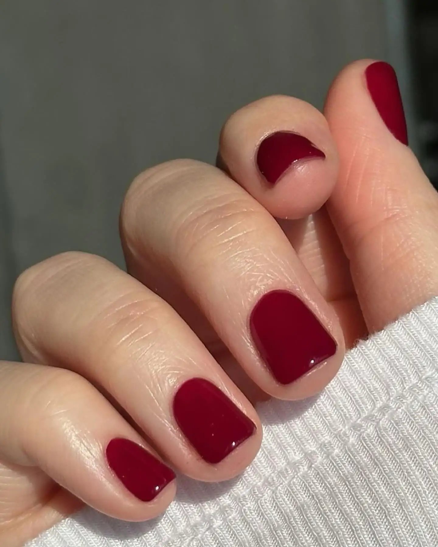 Una mano con uñas cortas pintadas de color bordó brillante apoya sus dedos sobre una tela acanalada blanca.