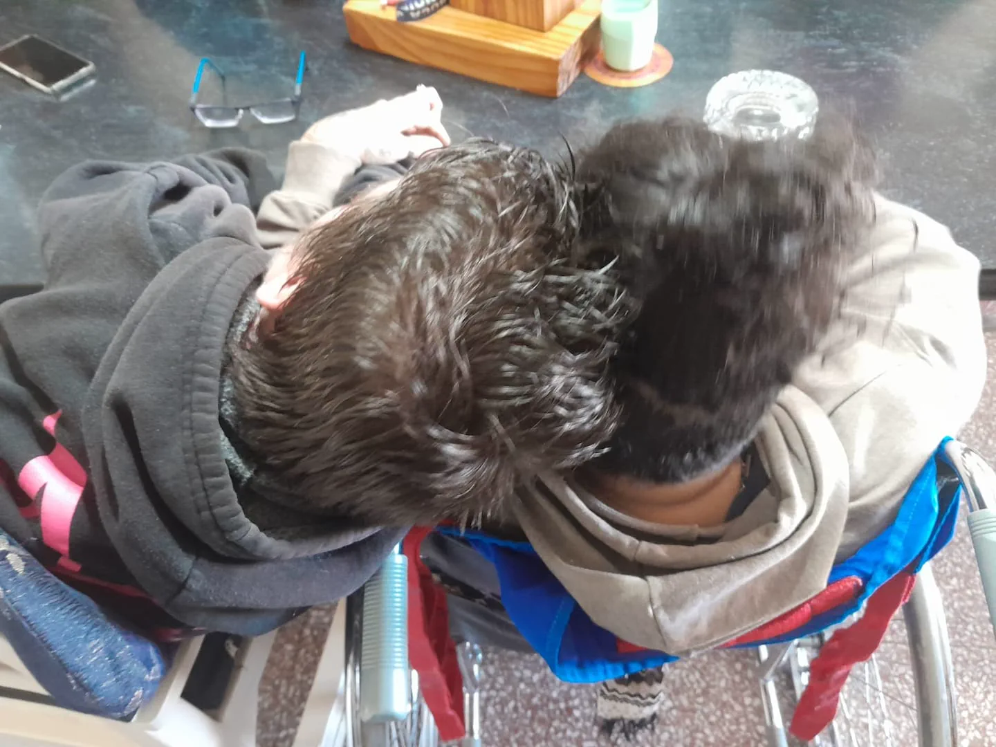 Dos personas sentadas juntas y vistas desde arriba apoyan sus cabezas una contra la otra.