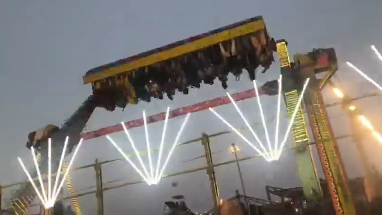 Un juego mecanico con personas sentadas en fila se balancea en el aire cerca de postes con luces.