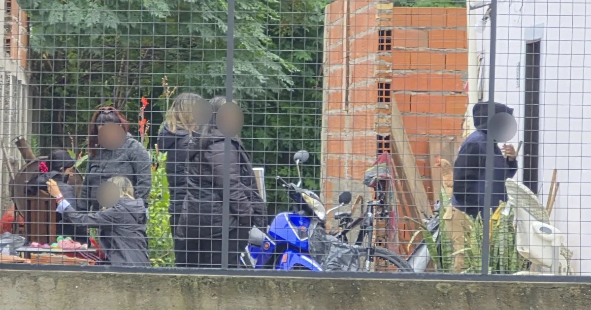 Varios vecinos con los rostros difuminados conversan detrás del enrejado de una casa junto a una moto azul.