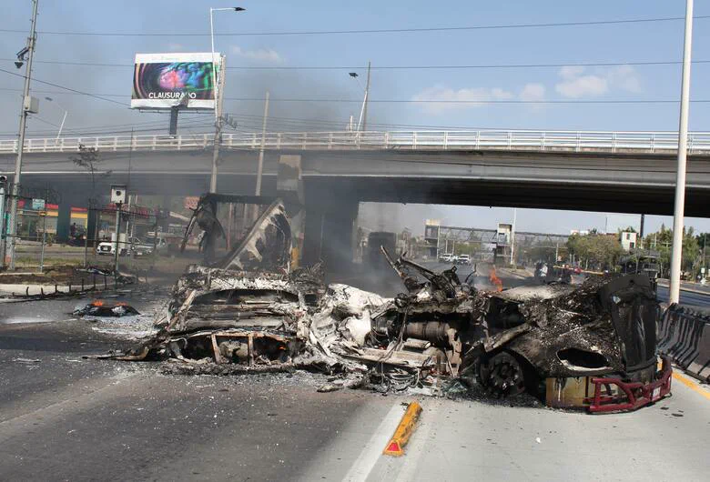 Vehículos totalmente quemados y destruidos bloquean una avenida debajo de un puente autopista.