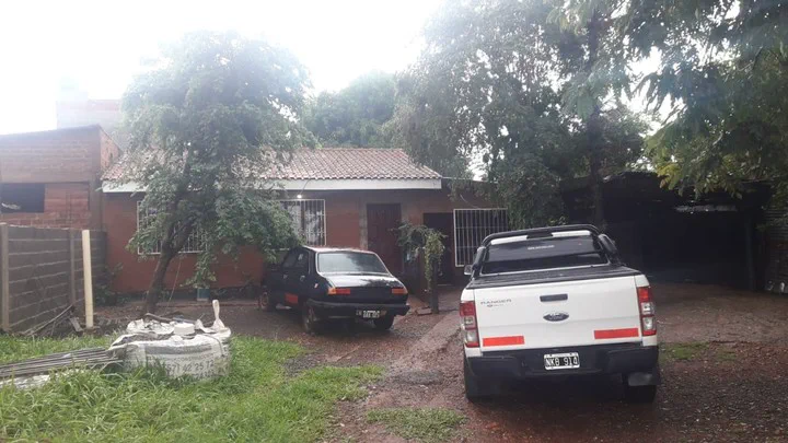Una camioneta blanca y un auto oscuro estacionados en la entrada de tierra de una casa con techo de tejas.