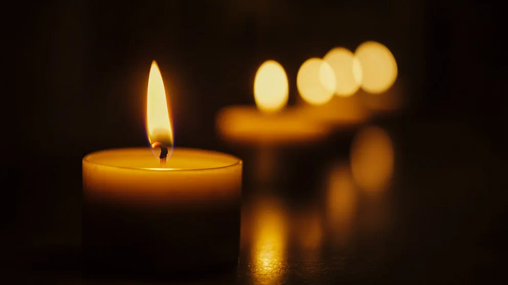 Vela encendida en primer plano con otras velas desenfocadas en fila detras.