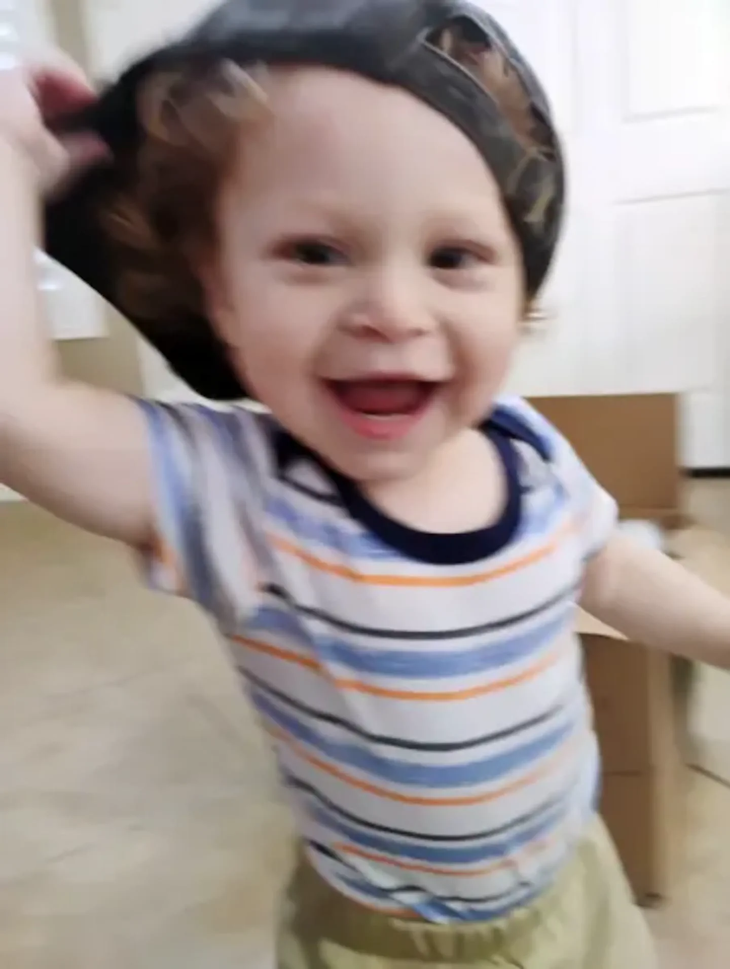 Nene chiquito sonriendo con una gorra puesta al revés y remera a rayas adentro de una casa.