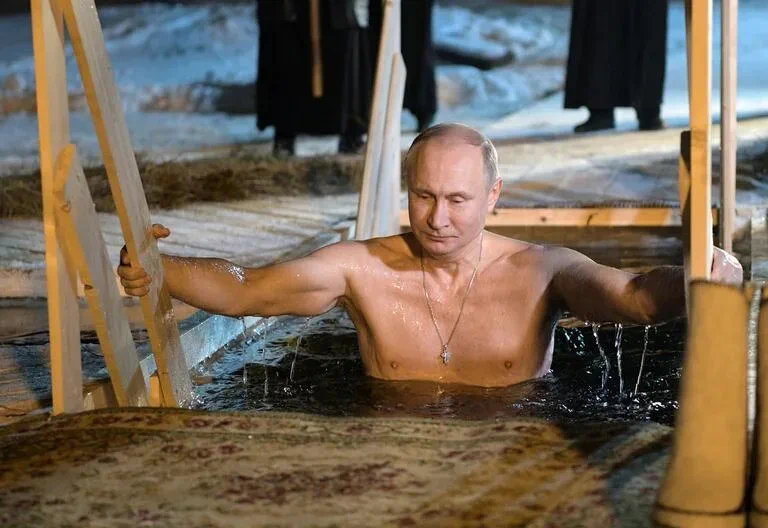 Vladimir Putin con el torso descubierto y una cruz en el pecho se sumerge en agua de noche.