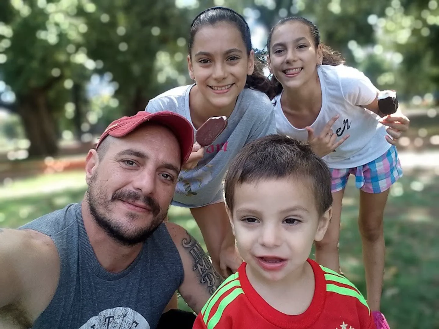 Un hombre y tres nenes se sacan una selfie sonriendo al aire libre mientras dos comen helado.